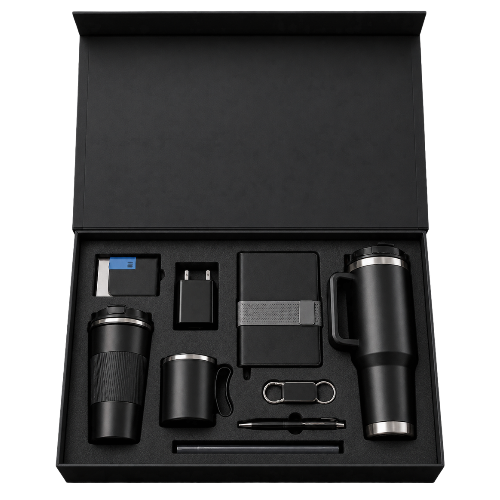 Top-down view of an open black magnetic gift box containing a vacuum tumbler, mug, notebook, pen, and tech accessories.