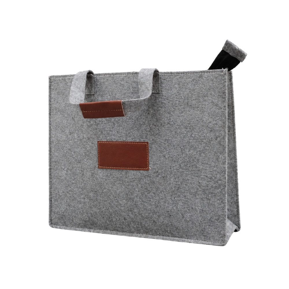 A grey felt tote bag with brown faux leather handle wraps and a blank rectangular branding patch on a white background.