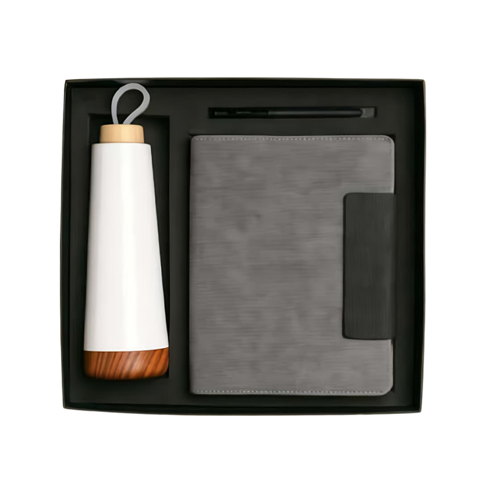 Top-down view of an executive gift set in a black box containing a white bottle with wood base, a grey notebook, and a pen.