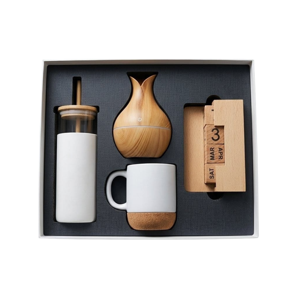 Top-down view of a corporate gift set in a black box containing a glass bottle, aroma diffuser, ceramic mug, and wooden calendar.