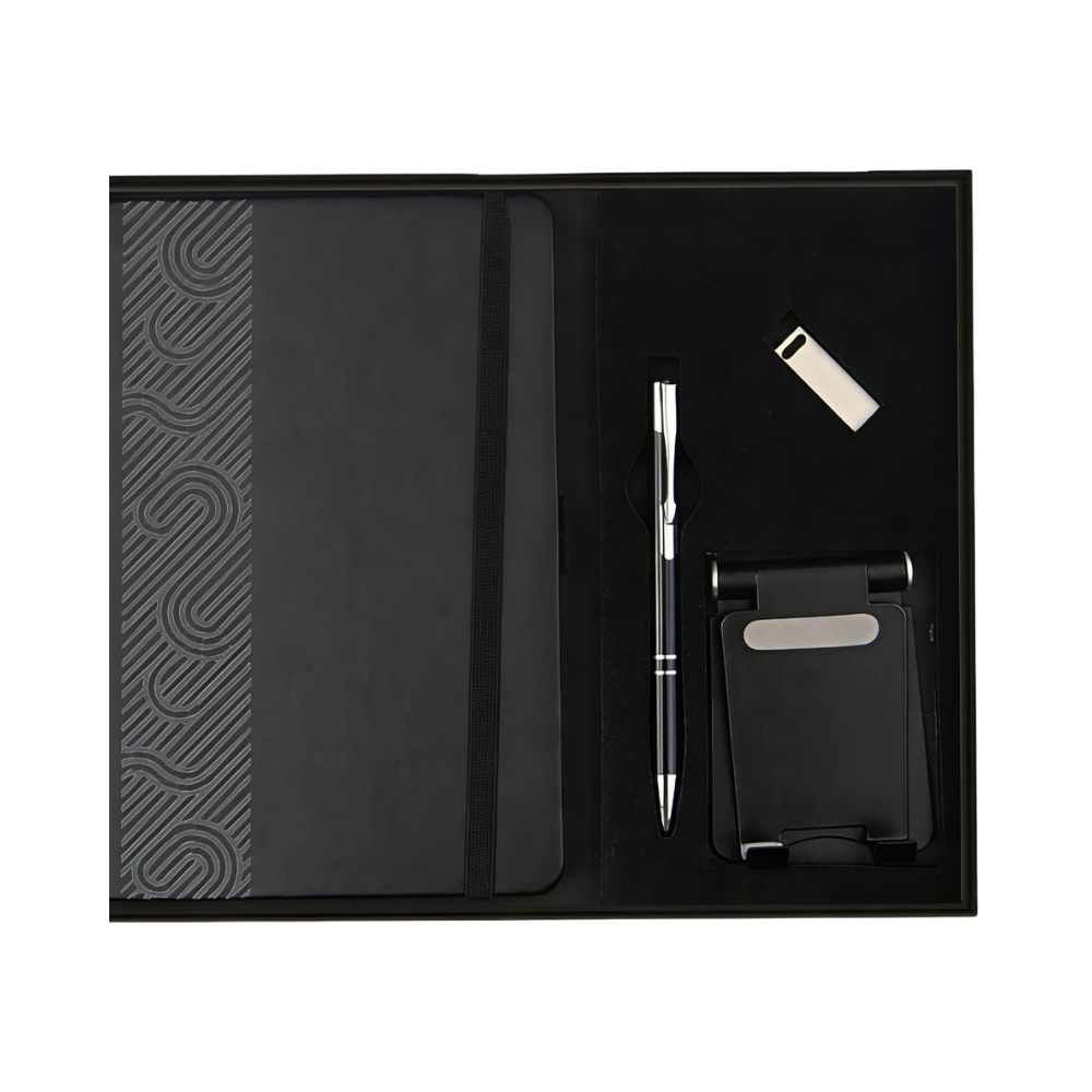 Top-down view of an executive gift set in a black box containing a patterned notebook, a silver-accented pen, a USB drive, and a foldable phone stand.