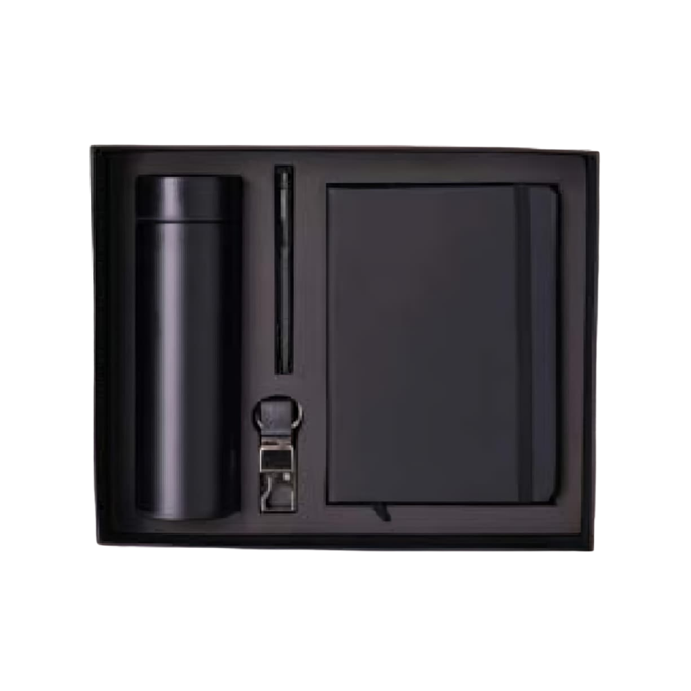 A top-down view of a 4-piece matte black executive gift set inside a presentation box, featuring a bottle, notebook, pen, and keychain.
