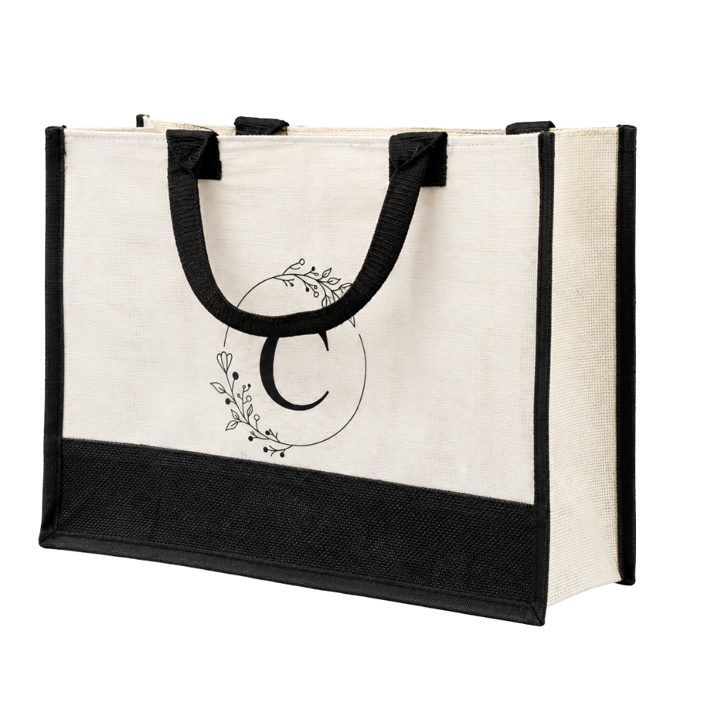 A beige jute tote bag with black trim and handles, featuring a black floral wreath monogram with the letter C on the front.